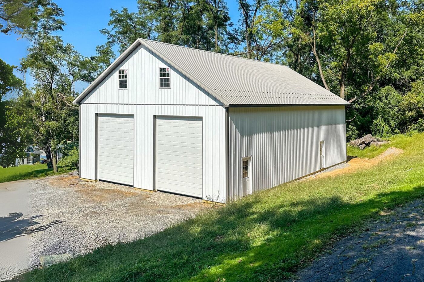 Corner of White Pole barn garage with view of two garage doors and attic windows